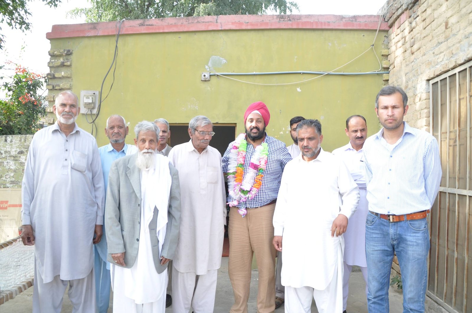 Dr Peter Chadha, in a turban and garland, standing with a group of residents outside a house in Bewal, November 2017